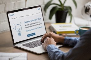 Person typing on a laptop displaying the Segovia Sí Innova 2026 information page with a lightbulb graphic on screen.