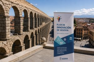Roman aqueduct of Segovia with a tall banner reading Plan de Innovación de Segovia in a sunny plaza.